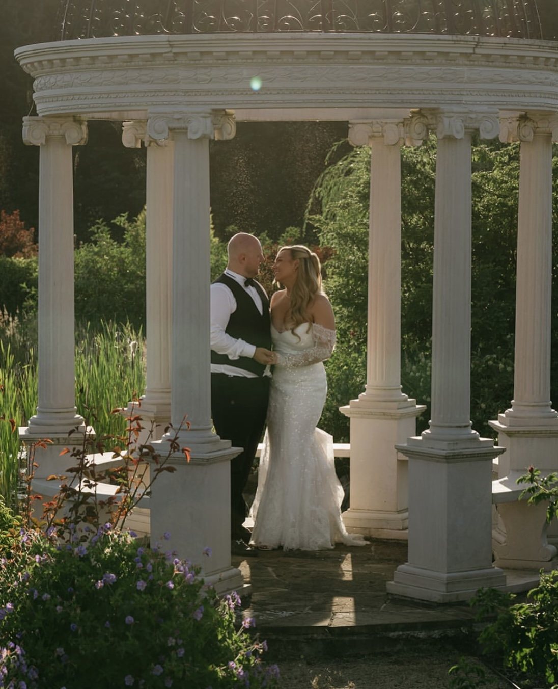 Bride and groom standing together beneath a garden gazebo