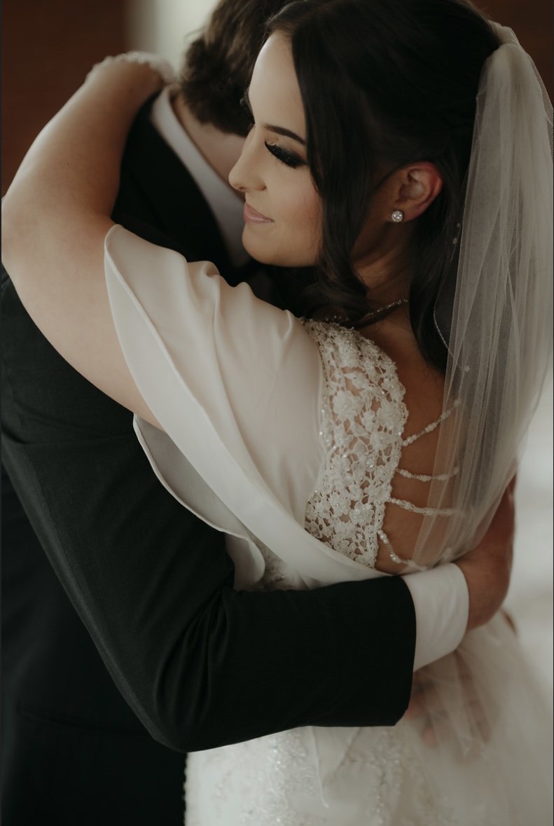 Bride embracing groom, wearing a lace wedding dress and veil